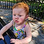 toddler, child, red_hair, outdoor, bench, curious, fruit_pattern, colorful_clothing, sunlight, park, fence, concrete, sidewalk, hand, face, expression, person, summer, nature, playground