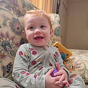 Nova joined the competition — help win amazing prizes! toddler, child, smiling, indoor, couch, onesie, patterned_clothing, toy, purple_ball, red_hair, happy, sitting, baby, drool, playful, home, comfort, cute, portrait, person