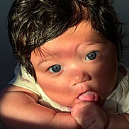 Avoni is registered to the contest to win money with this photo: baby, infant, face, blue_eyes, dark_hair, tongue, thumb, hand, cheeks, skin, closeup, portrait, sunlight, shadow, expression, onesie, cute, newborn, photography, indoor