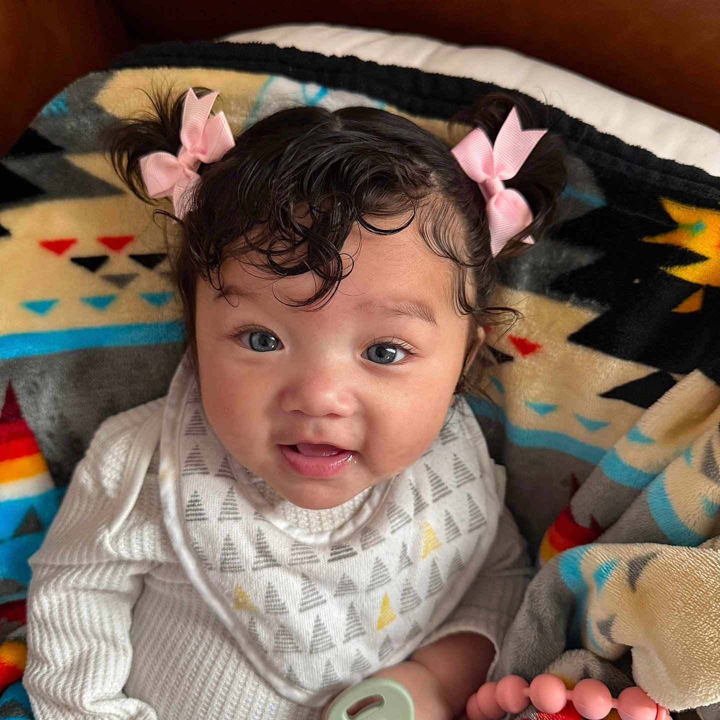 Avoni is registered to the contest to win money with this photo: baby, beaded_clip, bib, blanket, cheeks, child, colorful_pattern, couch, cozy, curly_hair, drool, hand, indoor, infant, onesie, pacifier, pigtails, pink_bow, portrait, smile