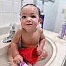 baby, child, toddler, bathtub, bathroom, water, wet, sitting, smiling, face, portrait, red_cup, bath_toy, bottle, skincare, faucet, tiles, indoor, bathing, happy