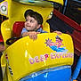 toddler, child, amusement_ride, yellow, blue, submarine, toy, indoor, play_area, smiling, face, hands, curious, seat, colorful, plastic, fun, entertainment, young, portrait