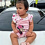 baby, child, pink_clothing, minnie_mouse, overalls, shoes, pony_tail, car, hood, traffic_lights, pedestrian_sign, outdoor, urban, curious, sitting, cute, portrait, person, daytime, casual
