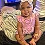baby, child, infant, girl, headband, bow, pink_dress, sitting, blanket, bed, indoors, soft_lighting, cute, chubby_arms, curly_hair, person, portrait, smile, skin, cozy