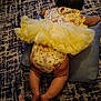 baby, tutu, yellow_clothing, onesie, cushion, carpet, floor, infant, barefoot, footwear, human_leg, patterned_rug, indoors, child, toddler, skin, laying_down, back_view, foot, sandal