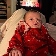 Harlee is registered to the contest to win money with this photo: baby, infant, child, red_dress, hand, face, person, indoor, bed, blanket, soft_lighting, background, blur, clothing, human, portrait, young_child, comfort, relaxing, warm