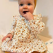 Luna a rejoint le concours — aidez-le/la à gagner de superbes lots ! baby, infant, child, portrait, headband, dress, patterned_dress, sitting, hand_in_mouth, blue_eyes, chubby_cheeks, feet, toes, indoor, bokeh_background, cute, teething, floral_pattern, skin, smile