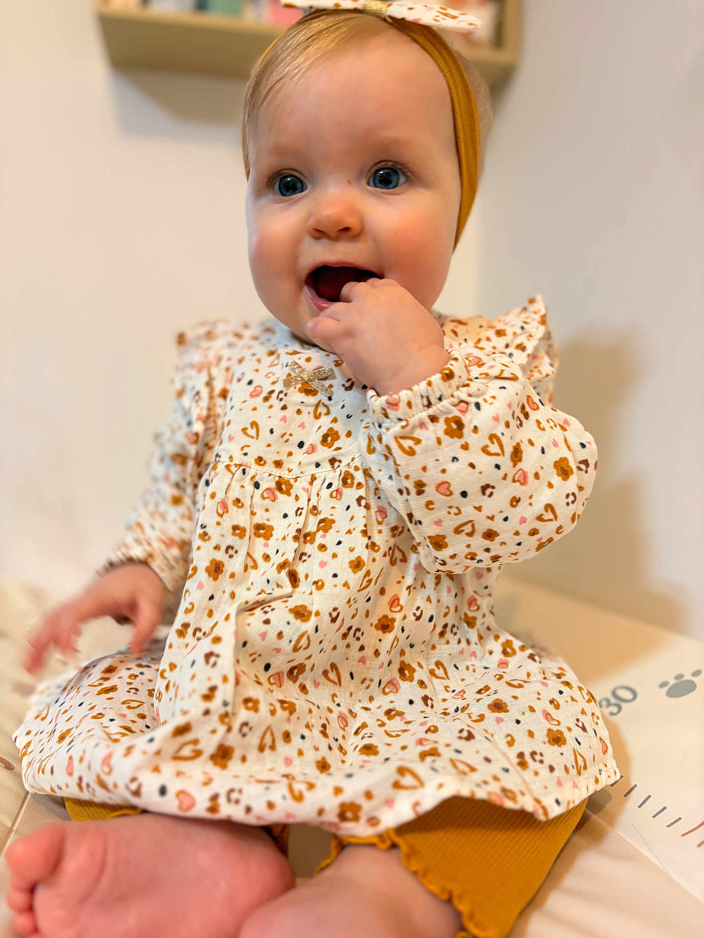 Luna a rejoint le concours — aidez-le/la à gagner de superbes lots ! baby, infant, child, portrait, headband, dress, patterned_dress, sitting, hand_in_mouth, blue_eyes, chubby_cheeks, feet, toes, indoor, bokeh_background, cute, teething, floral_pattern, skin, smile