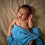 baby, infant, blue_blanket, lying_down, curly_hair, expression, closeup, skin, child, cute, soft_texture, blanket, comfort, indoors, newborn, portrait, face, hand, eyes, resting