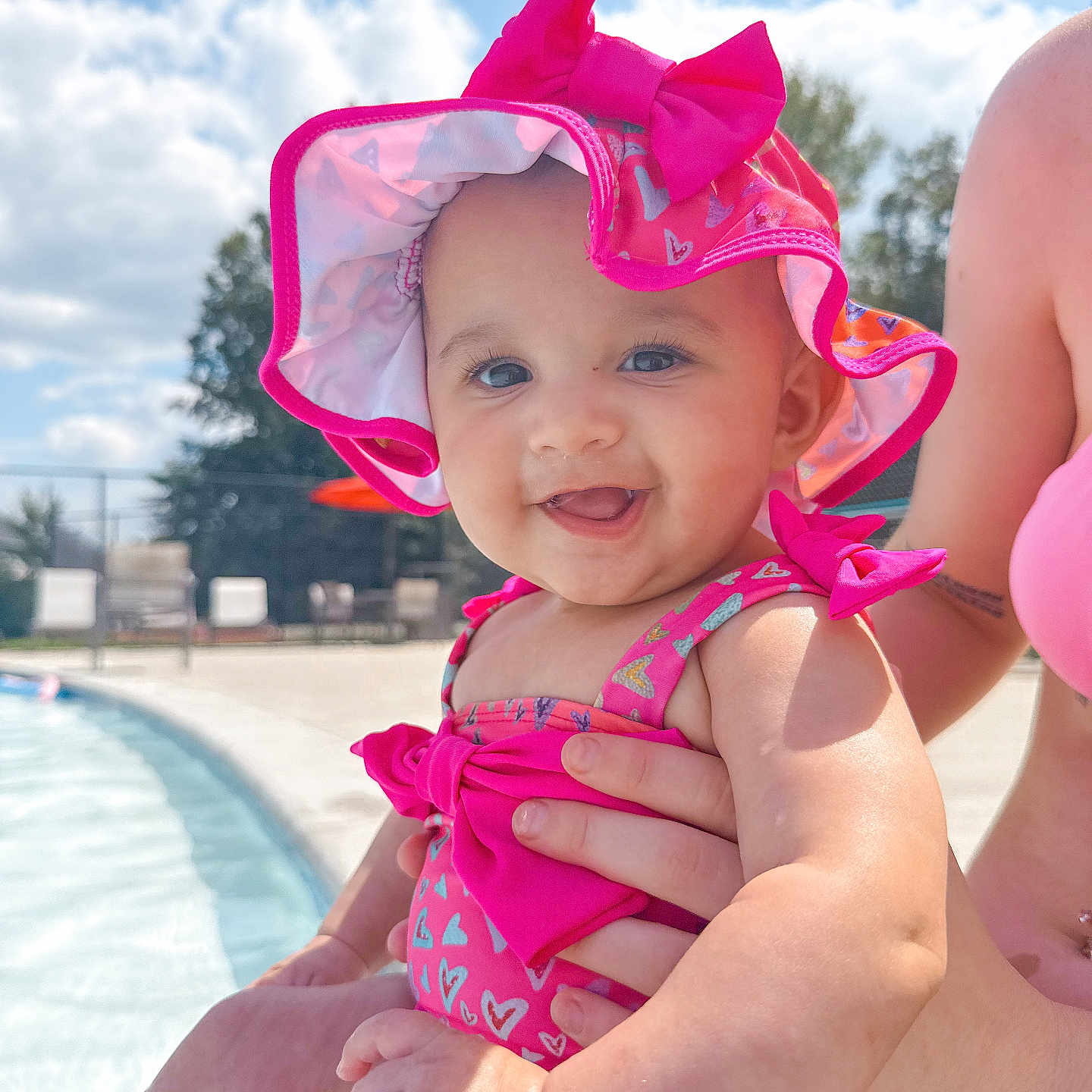 Londyn joined the competition — help win amazing prizes! adult_hand, baby, blue_sky, child, clouds, cute, daylight, happy, infant, outdoor, pink_hat, pink_swimsuit, poolside, portrait, skin, smiling, summer, sunny, vacation, water