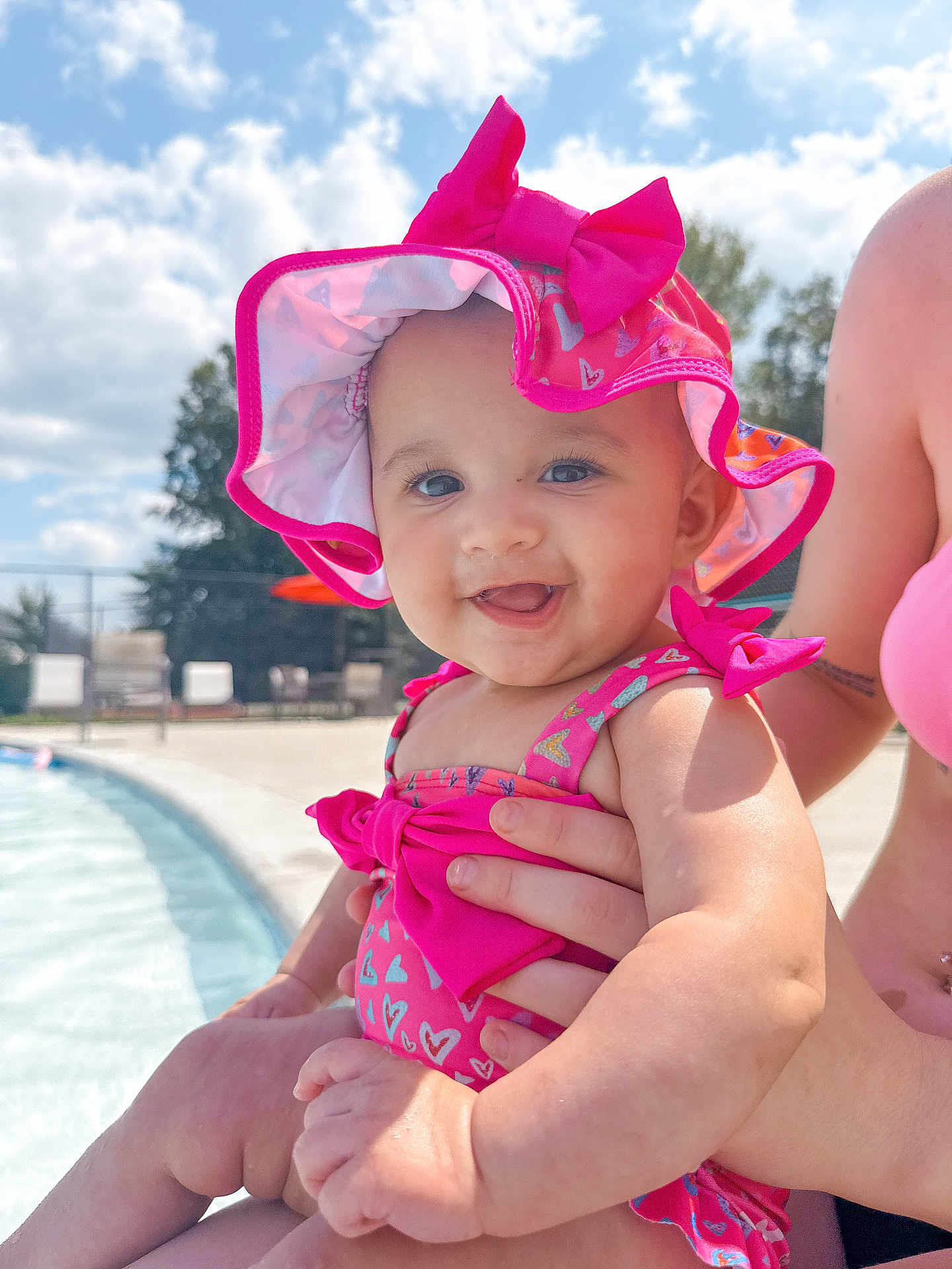 Londyn joined the competition — help win amazing prizes! baby, child, smiling, pink_hat, pink_swimsuit, poolside, outdoor, sunny, daylight, water, adult_hand, happy, summer, cute, portrait, infant, skin, blue_sky, clouds, vacation