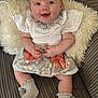 baby, smiling, couch, pillow, clothing, floral_skirt, bow, white_top, socks, cute, infant, happy, portrait, seated, indoor, child, person, soft_texture, striped_couch, cozy