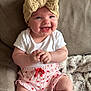 baby, infant, smiling, headband, bow, white_onesie, pink_shorts, strawberry_pattern, socks, couch, blanket, soft_fabric, happy, cute, child, indoors, portrait, sitting, skin, face