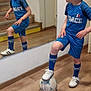 child, boy, soccer_ball, mirror, reflection, sportswear, blue_clothing, indoor, wooden_floor, stairs, socks, shoes, shorts, tshirt, sport, pose, home, casual, curly_hair, young