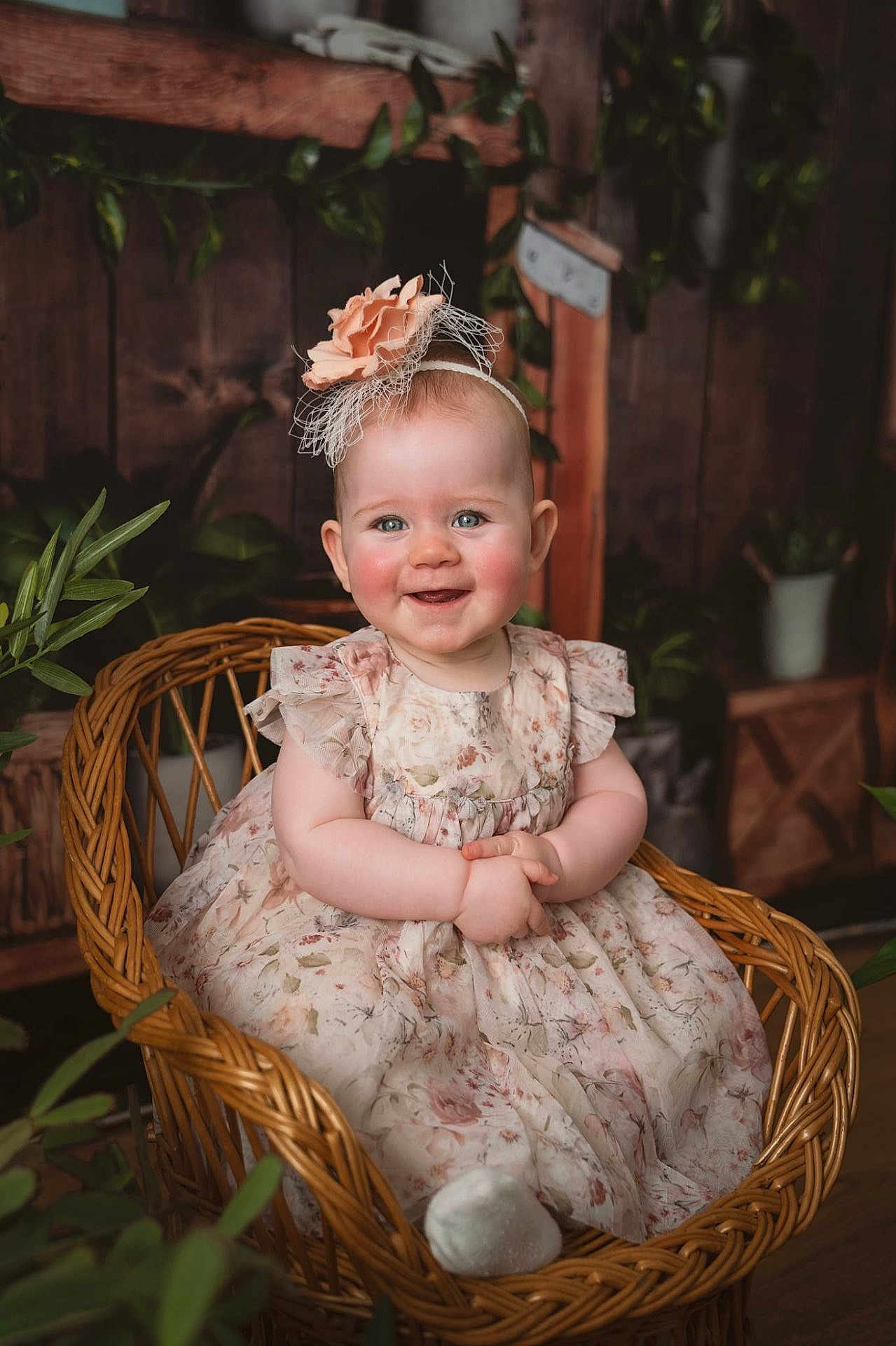 Ellie is registered to the contest to win money with this photo: baby, child, smiling, wicker_chair, floral_dress, headband, flower, rosy_cheeks, blue_eyes, indoor, plants, wooden_background, cute, portrait, sitting, happy, infant, decor, cozy, adorable