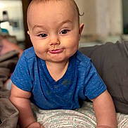 Ace is registered to the contest to win money with this photo: baby, child, blue_shirt, face, expression, skin, hair, blanket, indoor, furniture, person, infant, cute, portrait, hands, crawling, smirk, home, soft_light, casual