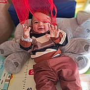 Julian a rejoint le concours — aidez-le/la à gagner de superbes lots ! baby, child, elephant_cushion, red_fabric, playful, smiling, indoor, soft_toy, measuring_mat, brown_pants, striped_sweater, happy, infant, cozy, cute, hands, face, lying_down, colorful, home