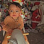 Julian a rejoint le concours — aidez-le/la à gagner de superbes lots ! baby, beaded_necklace, bright, child, christmas_tree, cute, decor, face, festive, floor_tiles, hand_holding, holiday_decorations, indoor, orange_outfit, person, rocking_horse, santa_figure, smiling, sparkles, toy