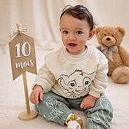 Julian a rejoint le concours — aidez-le/la à gagner de superbes lots ! age_marker, baby, child, cozy, cute, happy, indoor, lion_king_clothing, milestone, playful, portrait, sitting, smiling, socks, soft_carpet, studio, teddy_bear, toy, wooden_sign, young_child