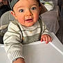 Julian participe au concours pour gagner de l'argent avec cette photo : baby, child, high_chair, cap, knitted_sweater, hand, face, blue_eyes, indoor, person, cute, curious, smile, infant, young_child, table, food_crumbs, home, casual, background_blur