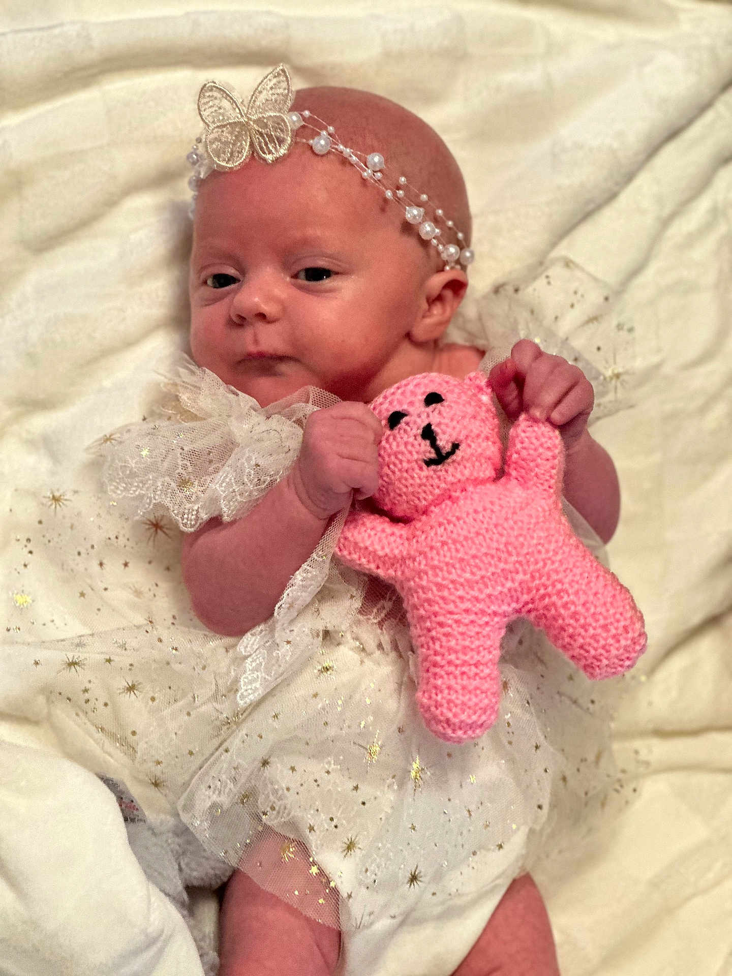 Lyla is registered to the contest to win money with this photo: baby, infant, headband, butterfly, pink_toy, knitted_toy, white_dress, lace, sparkles, cute, newborn, soft_blanket, portrait, smiling, hand, face, eyes, lying_down, child, adorable