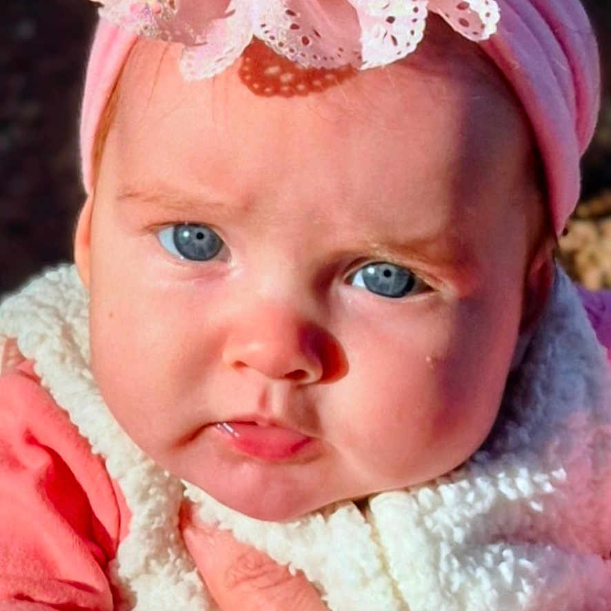 Serene joined the competition — help win amazing prizes! baby, blue_eyes, child, closeup, cute, expression, fleece, flower, hand, headband, holding, infant, natural_light, outdoor, person, pink, portrait, skin, vest, young