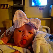 Serene is registered to the contest to win money with this photo: baby, newborn, hospital, blanket, bow, hat, tongue, hand, person, face, infant, cute, wrapped, bed, holding, indoor, lighting, nursery, portrait, hospital_room