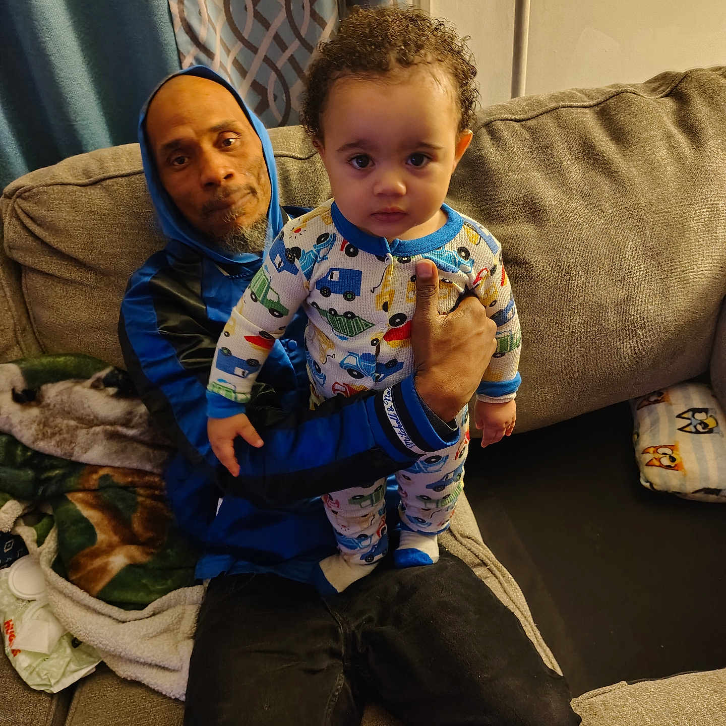 Rajai is registered to the contest to win money with this photo: blanket, casual, child, clothing, couch, cozy, curtains, expression, face, family, holding, home, indoor, man, pajamas, pattern, person, seated, sofa, toddler