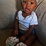 baby, child, sneakers, white_shirt, headband, couch, sitting, indoors, curious, cute, footwear, white_socks, texture, clothing, portrait, infant, expression, cozy, small_person, casual
