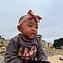 Infinity is registered to the contest to win money with this photo: baby, child, headband, sweatshirt, expression, outdoor, beach, rocks, cloudy_sky, person, cute, portrait, earrings, infant, smiling, hands, nature, daylight, casual_clothing, young_child
