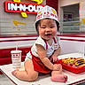 baby, child, smiling, table, food, fries, burger, cup, fast_food, restaurant, in_n_out, hat, name_tag, red_apron, indoor, high_chair, cute, chubby, person, happy