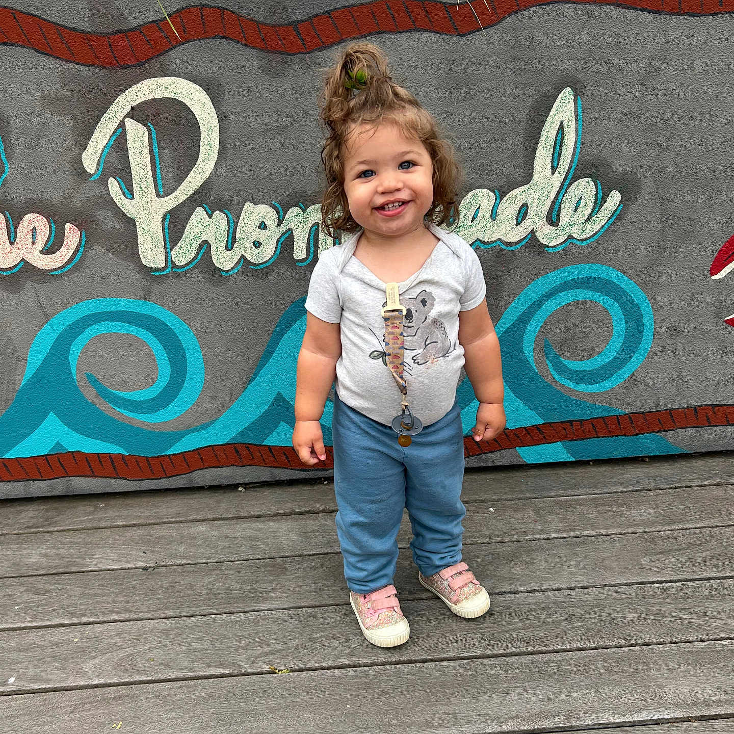 Jayley joined the competition — help win amazing prizes! blue_pants, casual_clothing, child, daylight, greenery, grey_shirt, hair_tied, happy, mural, outdoor, pacifier_clip, person, playful, smiling, sneakers, standing, toddler, urban, wall_art, wooden_floor