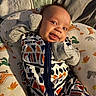 Micah joined the competition — help win amazing prizes! baby, infant, smile, face, clothing, onesie, pillow, dinosaur_pattern, handwear, mittens, fabric, bedroom, blanket, cute, portrait, child, indoors, soft_toys, happy, resting