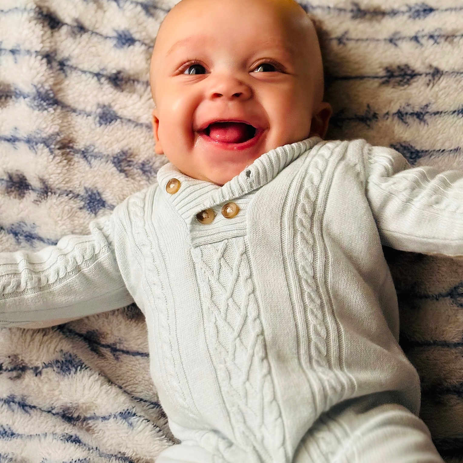 Micah is registered to the contest to win money with this photo: baby, smiling, infant, white_clothing, knitwear, blanket, soft_texture, happy, face, cute, lying_down, child, portrait, warm, cozy, indoors, expression, joyful, person, closeup