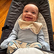 Micah joined the competition — help win amazing prizes! baby, smiling, infant, baby_chair, bib, blue_clothing, dinosaur_pattern, pants, happy, indoor, wooden_floor, seat, child, cute, portrait, young_child, soft_lighting, comfort, baby_toys, cozy