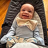 baby, smiling, infant, baby_chair, bib, blue_clothing, dinosaur_pattern, pants, happy, indoor, wooden_floor, seat, child, cute, portrait, young_child, soft_lighting, comfort, baby_toys, cozy