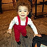 toddler, child, curly_hair, smiling, portrait, standing, red_overalls, white_shirt, indoor, carpet, adult, equipment_cart, black_bag, fashion, happy, front_view, flash_photography, brown_hair, baby, playful