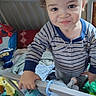 toddler, child, curly_hair, smiling, portrait, crib, nursery, bedroom, striped_shirt, baby, standing, toys, stuffed_animal, blanket, colorful, indoors, playful, face, furniture, happy