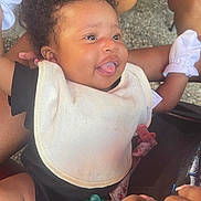 Nyielle is registered to the contest to win money with this photo: baby, bib, black_clothing, caregiver, child, close_up, curly_hair, dark_skin, family, hands, happy, infant, outdoor, pacifier, portrait, seated, smiling, stroller, tongue_out, white_clothing
