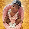 baby, infant, pink_basket, pink_clothing, lace, headband, curly_hair, wooden_floor, parquet, white_socks, sitting, indoors, cute, child, person, portrait, young_child, soft_texture, cozy, comfortable