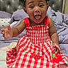 baby, child, smiling, happy, dress, red_dress, hair_bows, curly_hair, bed, bedding, pillow, tufted_headboard, indoor, cute, portrait, sitting, reaching_out, infant, person, cheerful