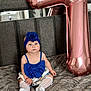 baby, blue_outfit, headband, flower_accessory, balloon, rose_gold, number_seven, bed, gray_bedspread, child, sitting, cute, indoor, portrait, celebration, decor, sock, white_sock, infant, fashion