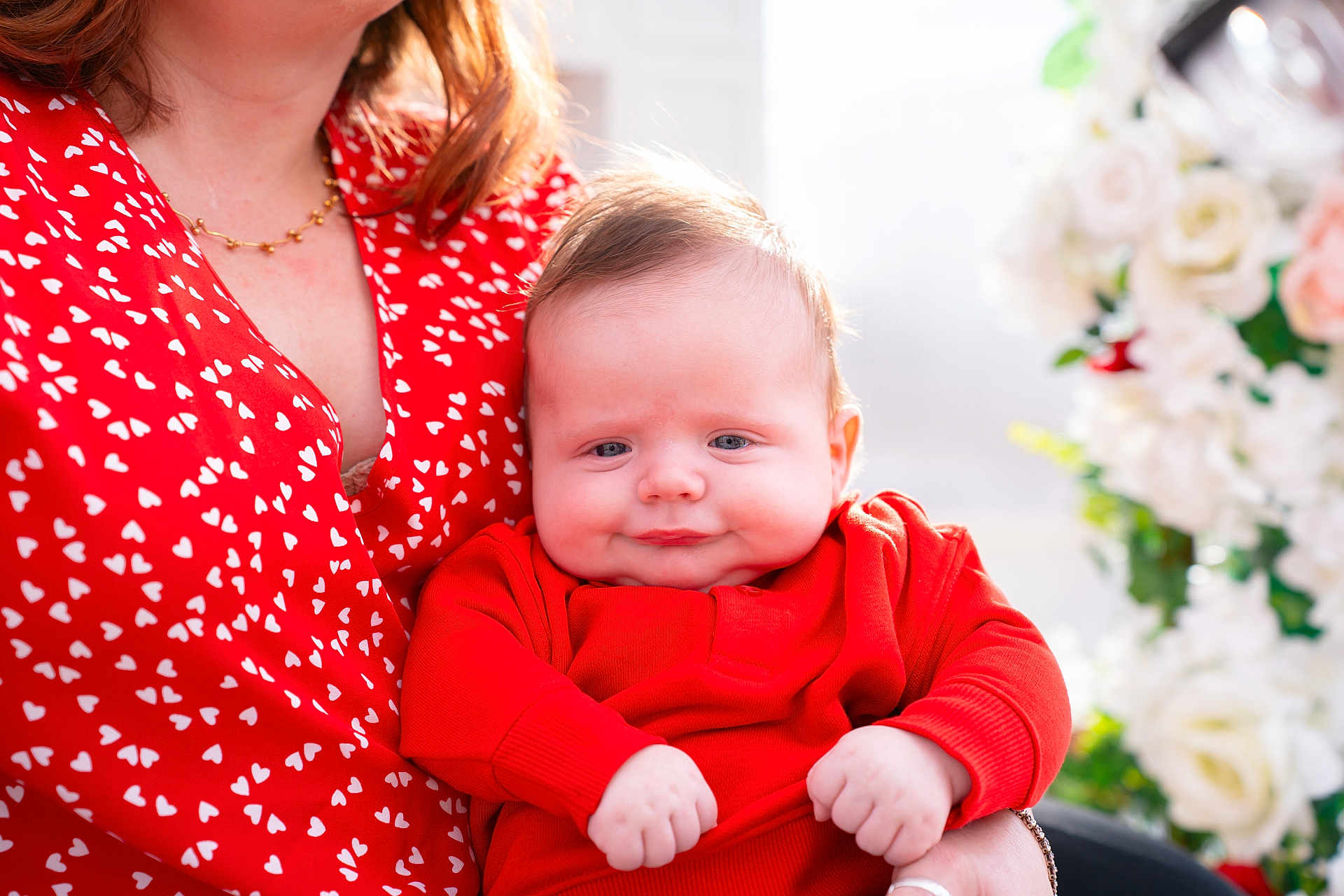 Daniel joined the competition — help win amazing prizes! baby, infant, woman, adult, red_clothing, red_dress, heart_pattern, holding, portrait, close_up, smile, chubby_cheeks, floral_background, necklace, hand, skin, cozy, indoor, natural_light, parenting