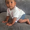 toddler, child, crawling, white_shirt, denim_shorts, gray_couch, indoor, curly_hair, person, furniture, decor, reflection, home, casual, portrait, cute, baby, skin, expression, hands