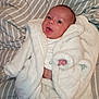 Tommy is registered to the contest to win money with this photo: baby, infant, face, tongue_out, white_robe, blanket, striped_bedspread, cute, newborn, soft_texture, lying_down, child, skin, hand, foot, indoors, expression, sleepwear, cozy, warm