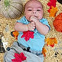 baby, infant, oats, knitted_pumpkin, autumn_leaves, blue_shirt, gray_pants, hand, face, smiling, lying_down, floor, fall, seasonal, cute, child, portrait, indoors, soft_texture, cozy