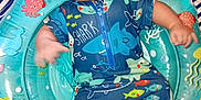Tommy joined the competition — help win amazing prizes! baby, infant, inflatable_ring, swimwear, shark_pattern, sea_creatures, dog_paw, striped_blanket, blue, colorful, cute, child, playful, indoor, person, clothing, sitting, portrait, looking_up, expression