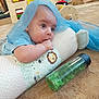 baby, infant, pillow, blue_cloth, hand, chewing, toys, wooden_toy, floor, carpet, green_bottle, animal_print, cute, curious, child, indoors, soft, play_area, person, young_child
