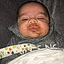 baby, infant, face, food_smear, blanket, hoodie, sleepy, cozy, indoor, closeup, child, cute, soft_texture, expressionless, lying_down, person, newborn, clothing, resting, comfort