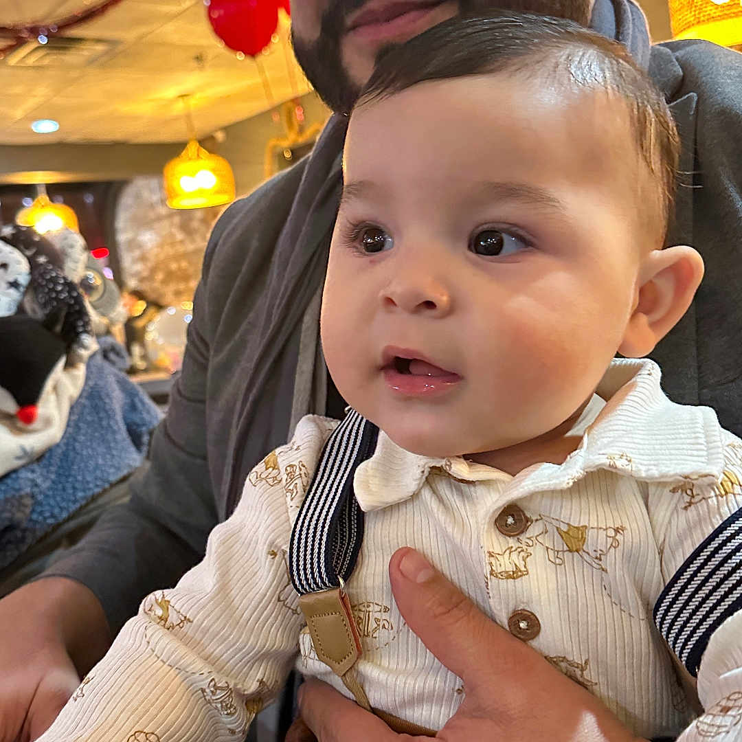 Emilio joined the competition — help win amazing prizes! baby, background, balloons, beard, celebration, clothing, curious, event, face, hand, holding, indoor, lighting, man, people, portrait, smile, suspenders, table, warm_light